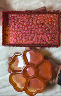 Two trinket holders, one a rectangle tray reddish with textured bottom. The second are several hearts to organize trinkets in a orange hue that shifts color in the light,